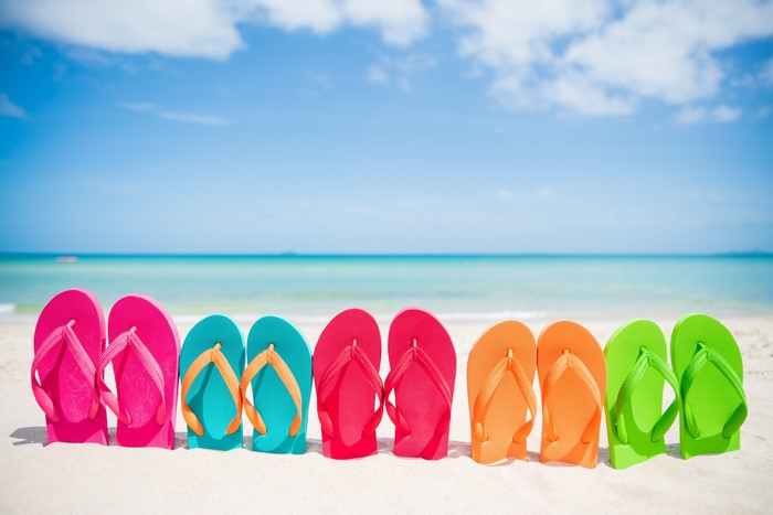 Multicolor flip-flops on a sandy beach with ocean and sky