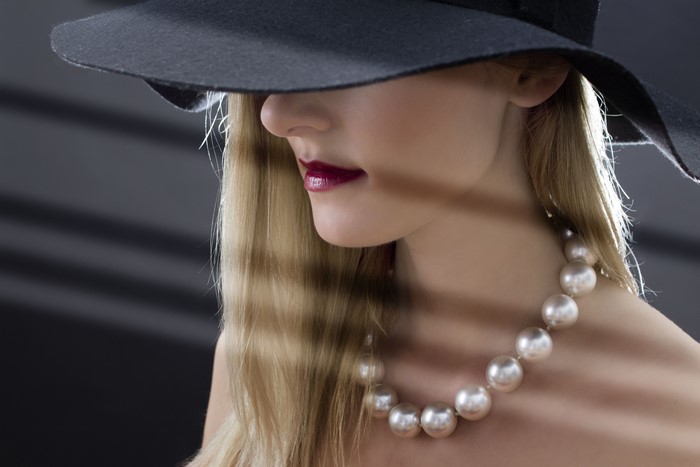 Blonde woman wearing a black hat and pearl necklace