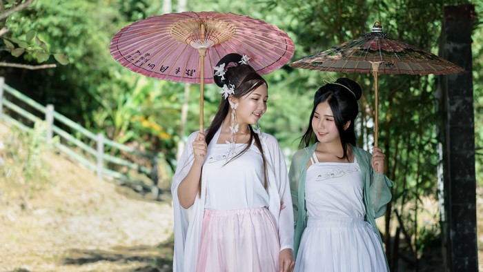 Two Asian women in traditional clothing holding umbrellas