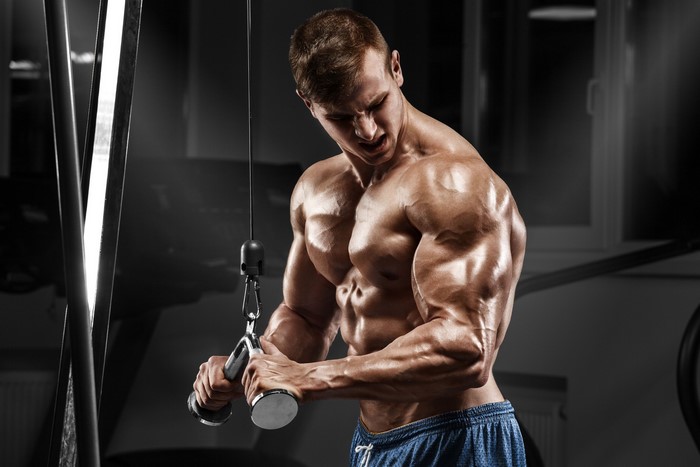 Muscular man performing triceps exercise with cable machine