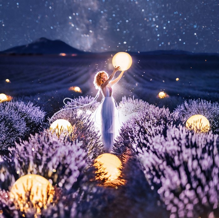 Woman holding a glowing ball in a lavender field at night