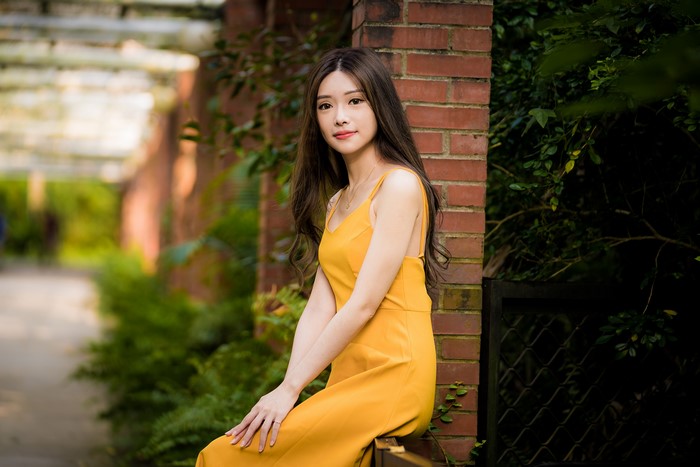 Asian woman in yellow dress sitting near brick wall