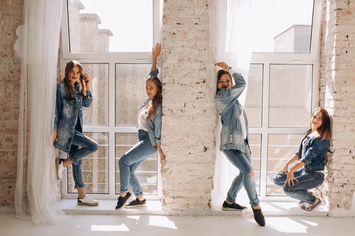 Four young women in denim outfits posing by a window