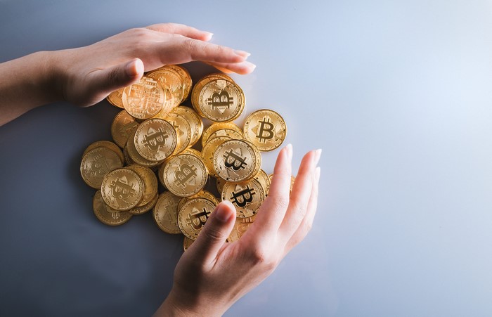 Hands protecting a pile of Bitcoin coins