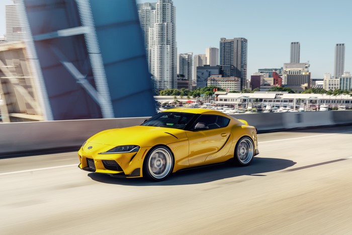 Yellow Toyota Supra driving on a highway with city skyline
