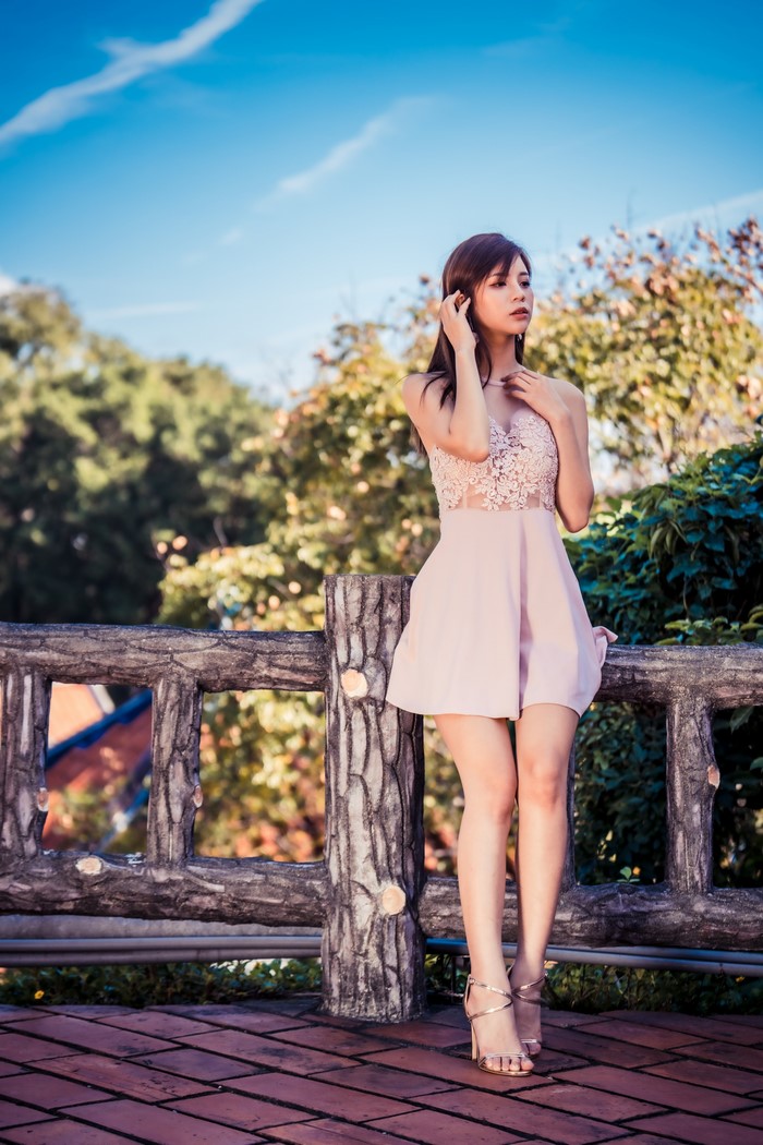 Asian woman in pink dress standing by a fence