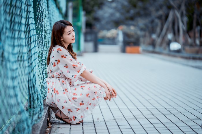 Asian woman in floral dress sitting by fence