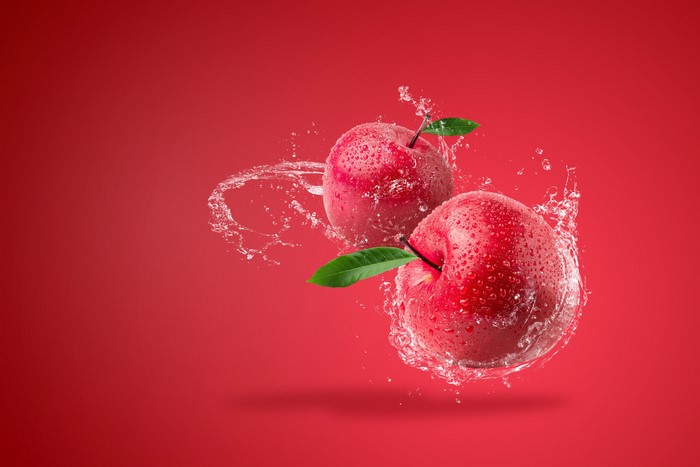 Two red apples with water splashes on red background