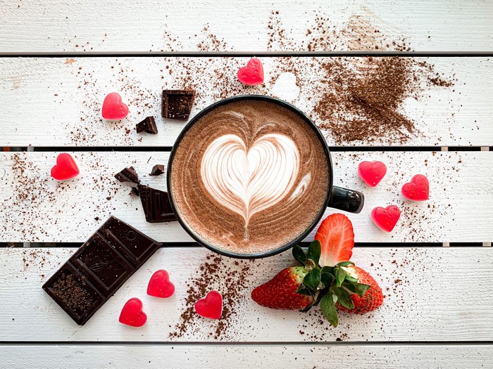 Hot chocolate with latte art, chocolate, strawberries, and heart candies