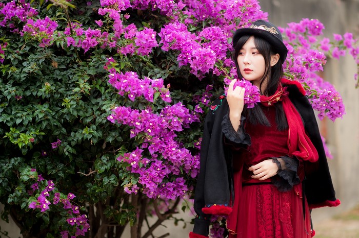 Asian woman in red dress and hat near bougainvillea