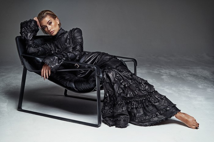 Hailey Baldwin in black dress sitting on armchair
