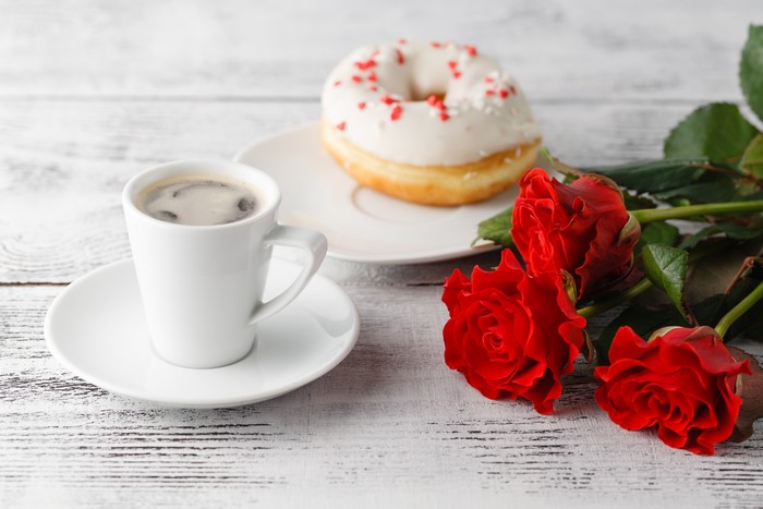 Coffee cup, donut, and red roses on a wooden table