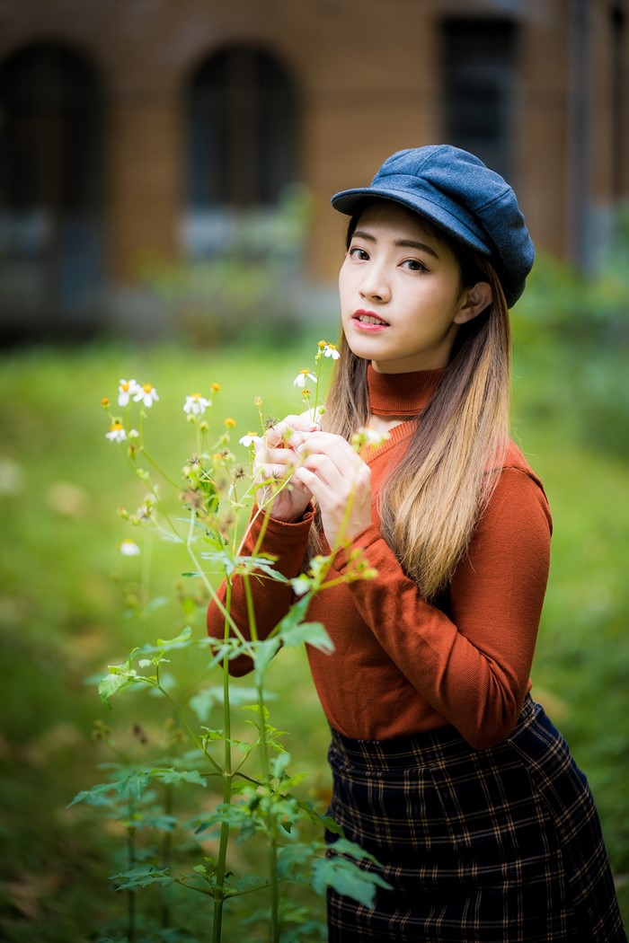 Asian woman in sweater and hat near flowers