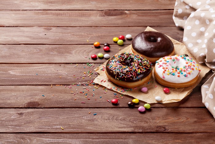 Three donuts with sprinkles and candies on wooden planks