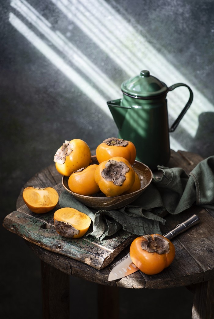 Persimmons on a wooden table with a green pitcher
