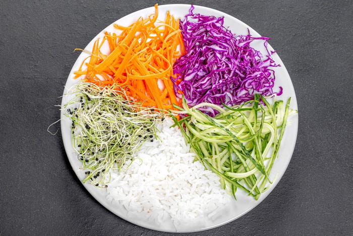 Plate of rice with shredded carrots, cabbage, sprouts, and cucumbers
