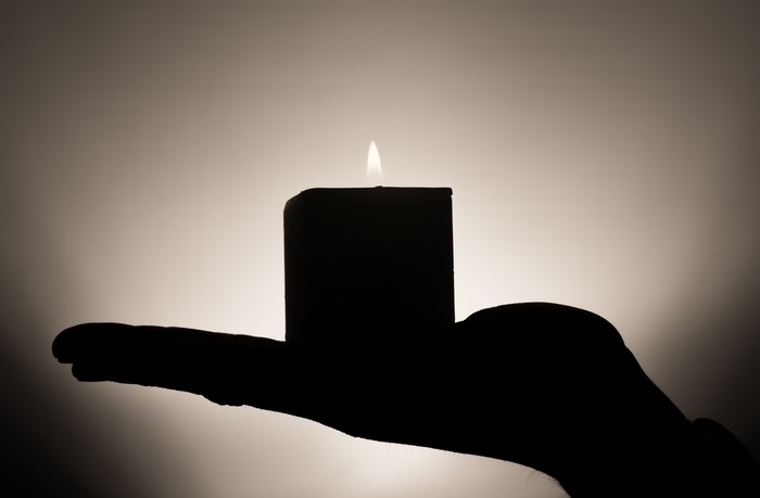 Silhouette of a hand holding a lit candle