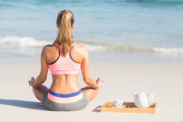 Woman meditating on beach with tea set
