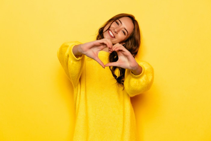 Woman in yellow sweater making heart gesture