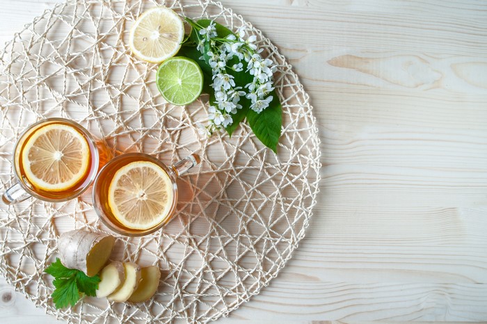 Two cups of tea with lemon, ginger, lime, and flowers