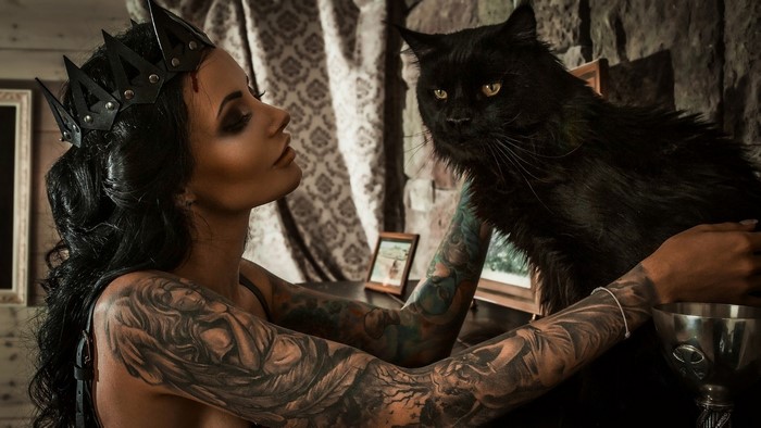 Brunette woman with crown and tattoos holding a black cat