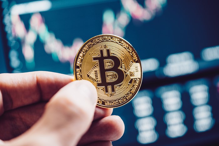 Bitcoin coin held in hand with stock chart background