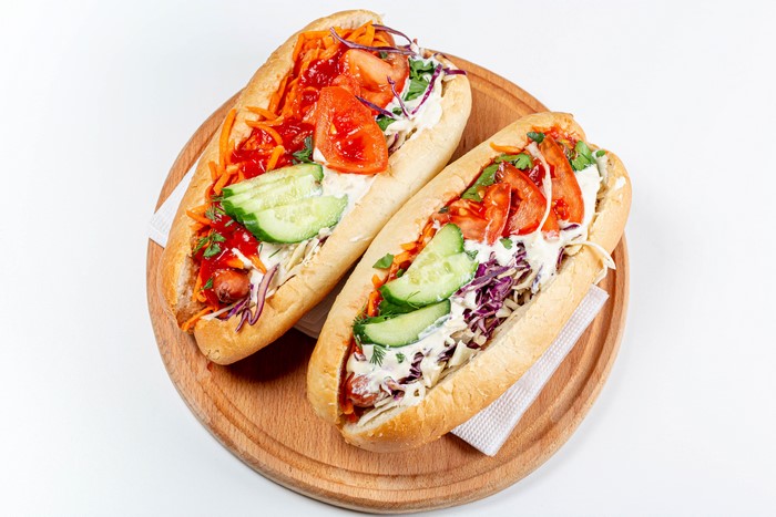 Two hot dogs with vegetables on a cutting board