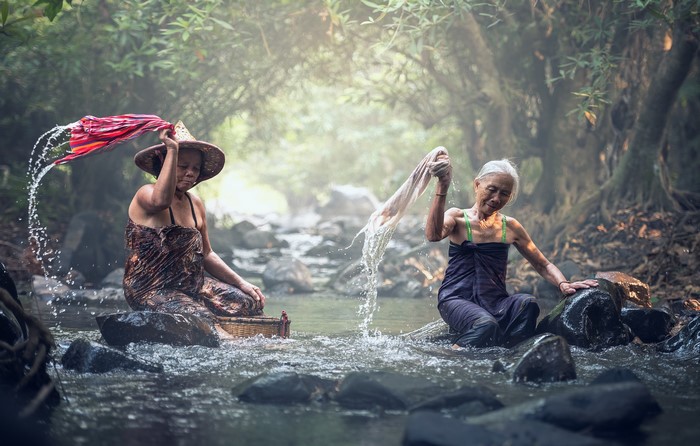 Two elderly Asian women washing clothes in a stream