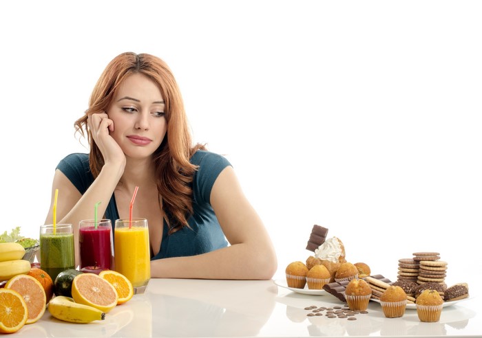 Woman choosing between healthy juices and unhealthy pastries