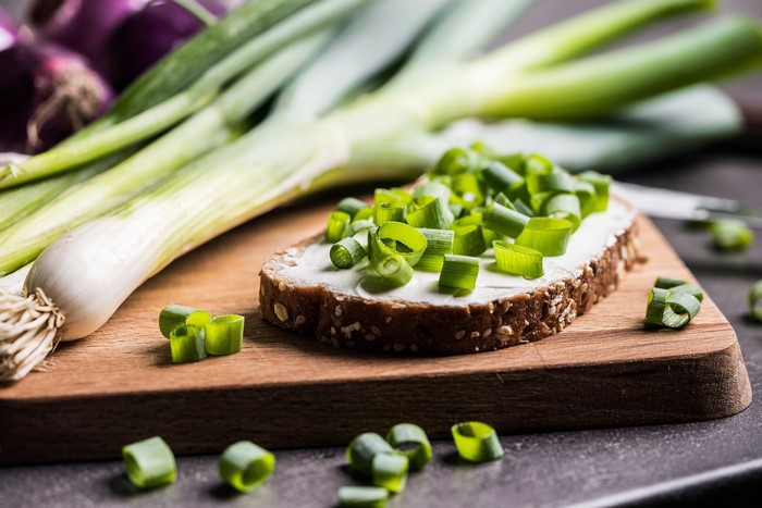 Scallions on bread with cream cheese on cutting board
