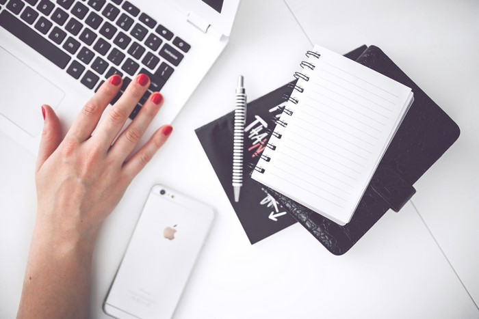 Woman's hand on laptop with iPhone and notepad