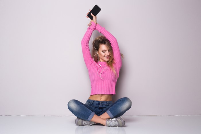 Woman in pink sweater and jeans listening to music