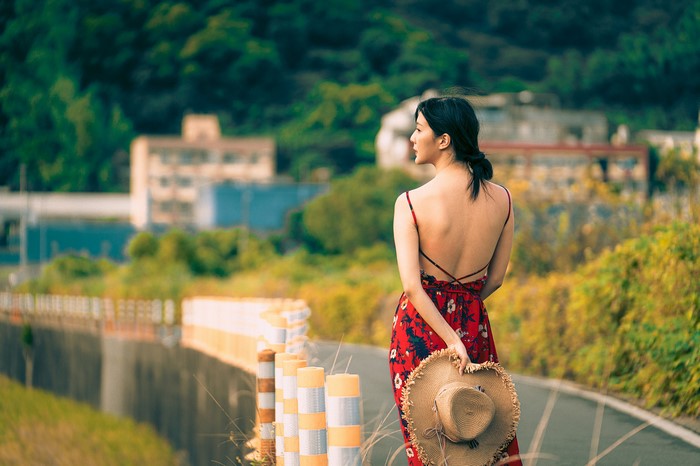 Brunette girl in red dress holding hat, back view