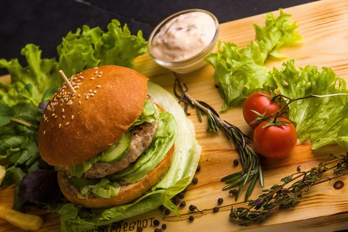 Hamburger with lettuce, tomatoes, and dip on a cutting board