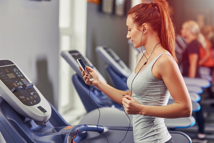 Redhead girl with headphones on treadmill in gym