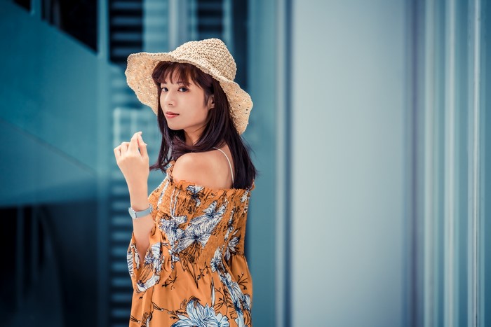 Asian woman with brown hair wearing a straw hat and floral off-the-shoulder blouse