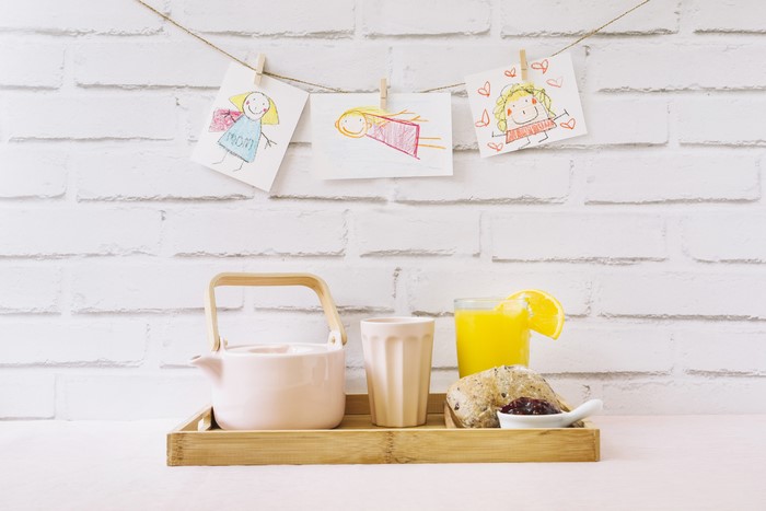 Breakfast tray with kettle, juice, pastry, and children's drawings