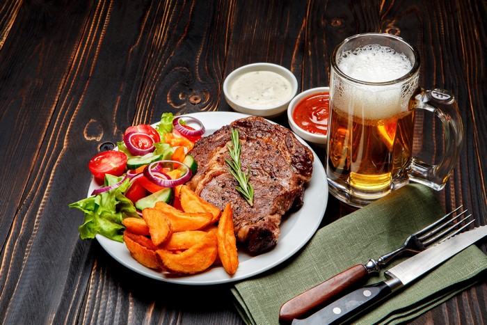 Steak, Fries, Salad, and Beer on Wooden Table
