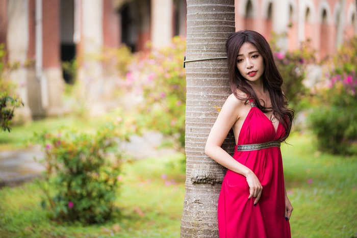Asian woman in red dress posing by tree