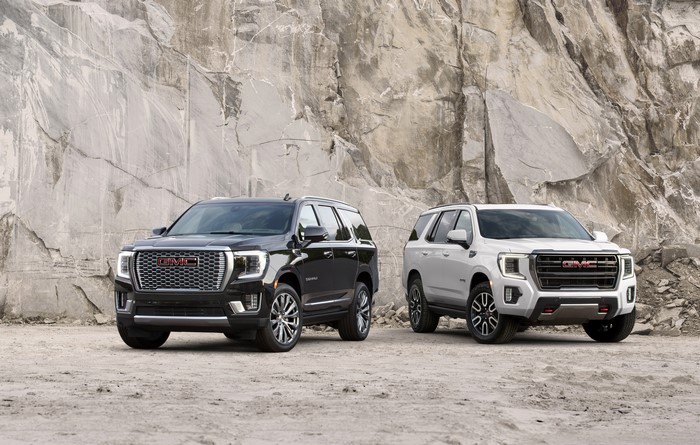 Two GMC Yukon SUVs, Black and White, in front of a rocky cliff