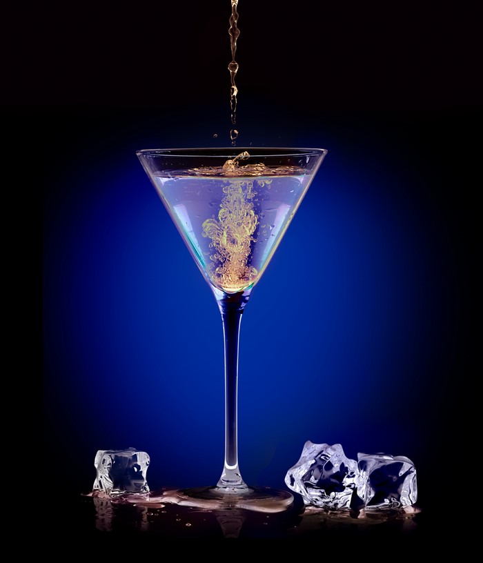 Cocktail being poured into a martini glass with ice