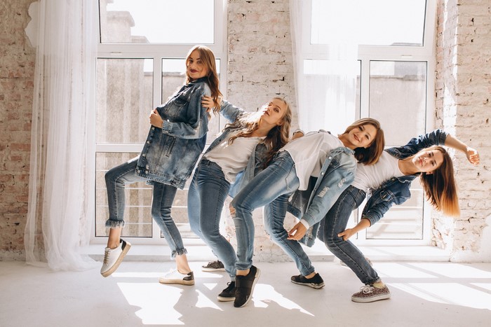 Four young women in denim outfits dancing