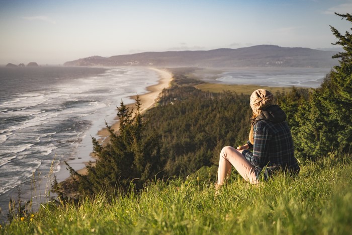 Woman in winter hat sitting on grass overlooking sea coast