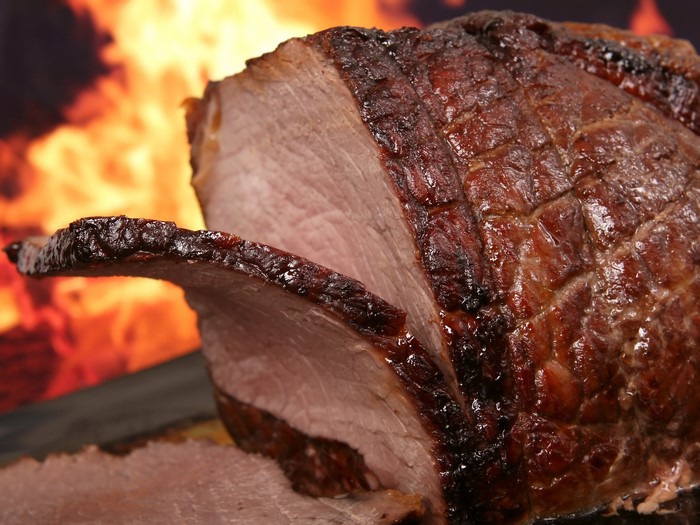 Close-up of a roasted ham with flames in the background