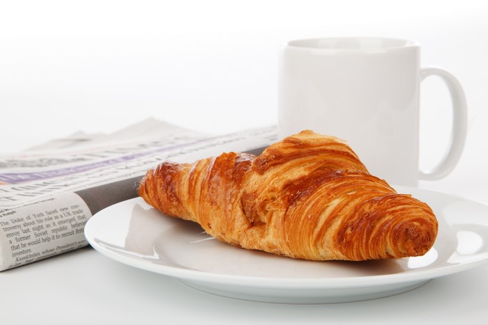 Croissant on a plate with a mug and newspaper
