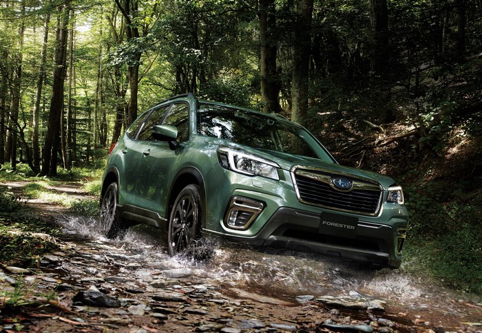 Green Subaru Forester driving through forest stream