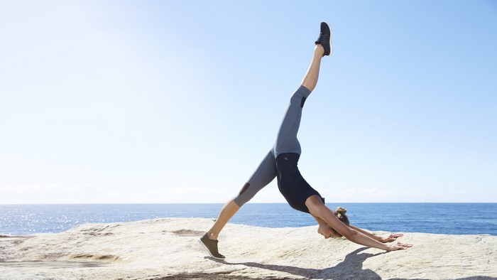 Woman doing yoga pose on rocks by the ocean