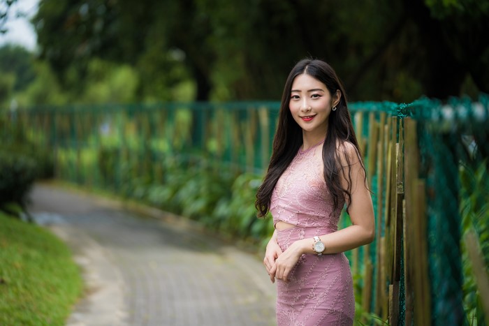 Asian woman in pink dress standing by a fence