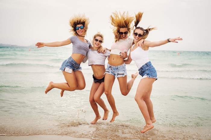 Four young women in shorts jumping on a beach