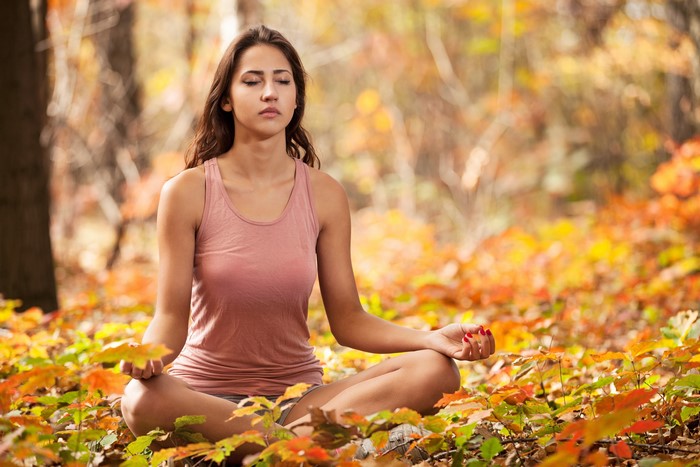 Woman meditating in Lotus position in autumn foliage